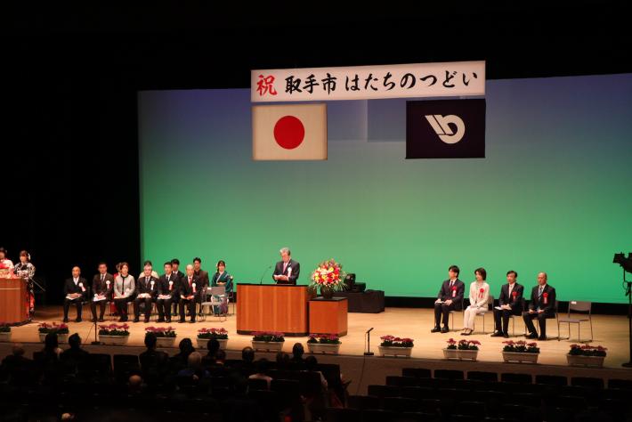 壇上で男性が着座の参加者にむけて挨拶をしている。
